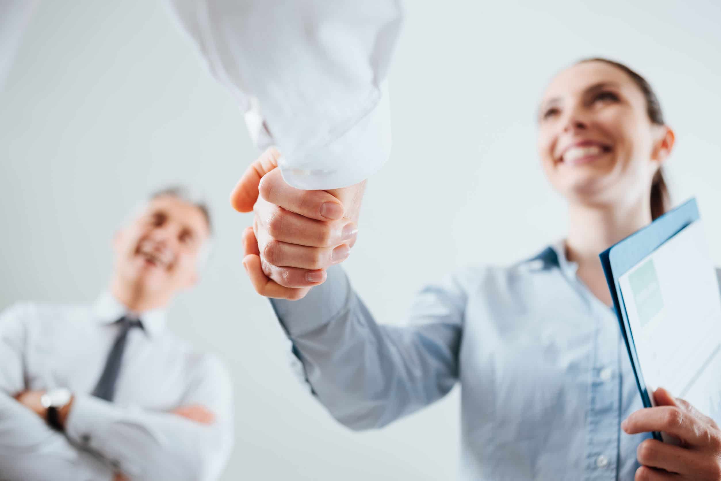 close-up of a woman and man shaking hands while a coworker looks on