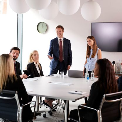 six office workers gathered around a conference table discussing business