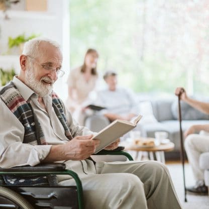 smiling elderly man seated in a wheelchair reading a book