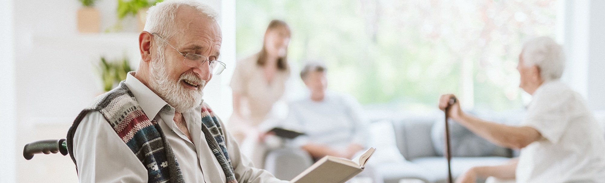 smiling elderly man seated in a wheelchair reading a book