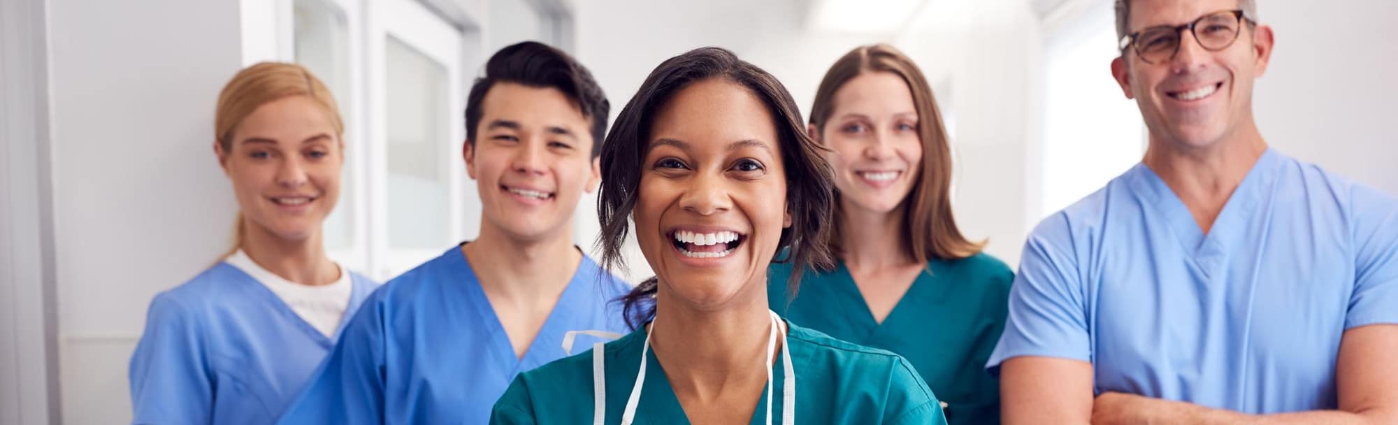 smiling woman with clipboard standing with three smiling medical coworkers in background