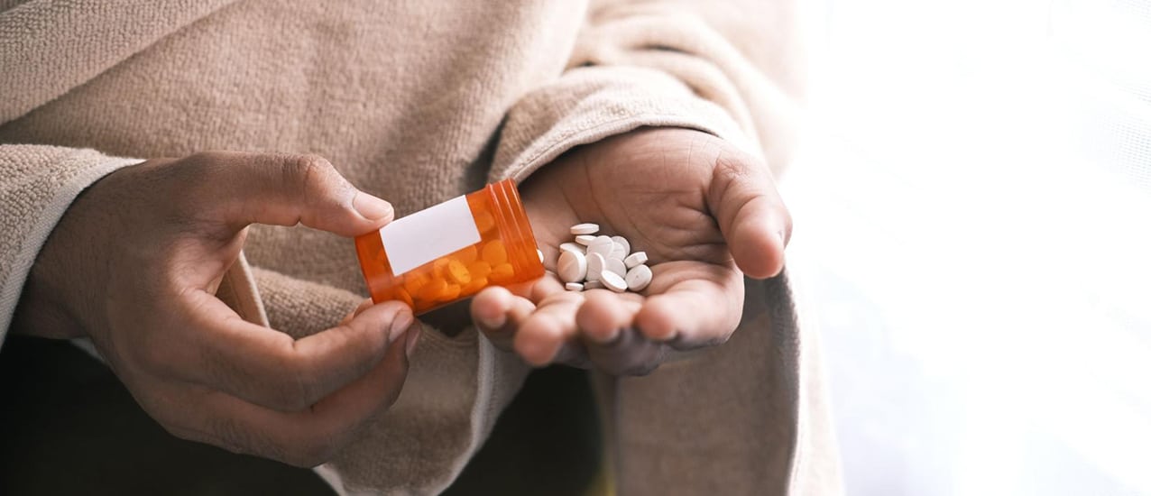 Close-up of the hands of a patient pouring pills from a prescription bottle.