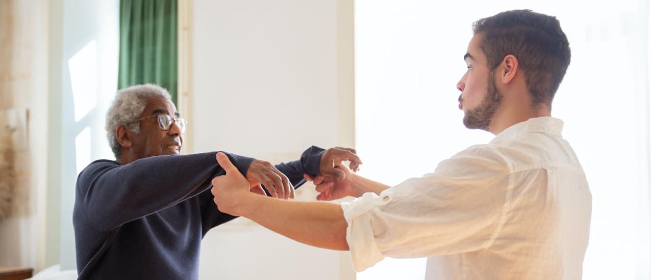 A healthcare worker helps a patient safely stand up from a hospital bed.