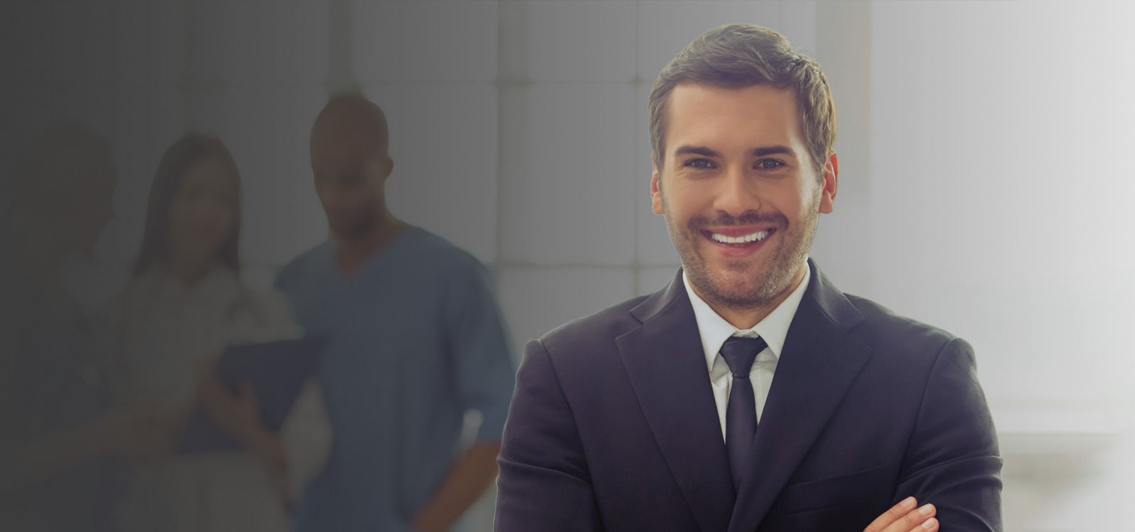 A smiling man wearing a suit stands next to a team of healthcare workers.